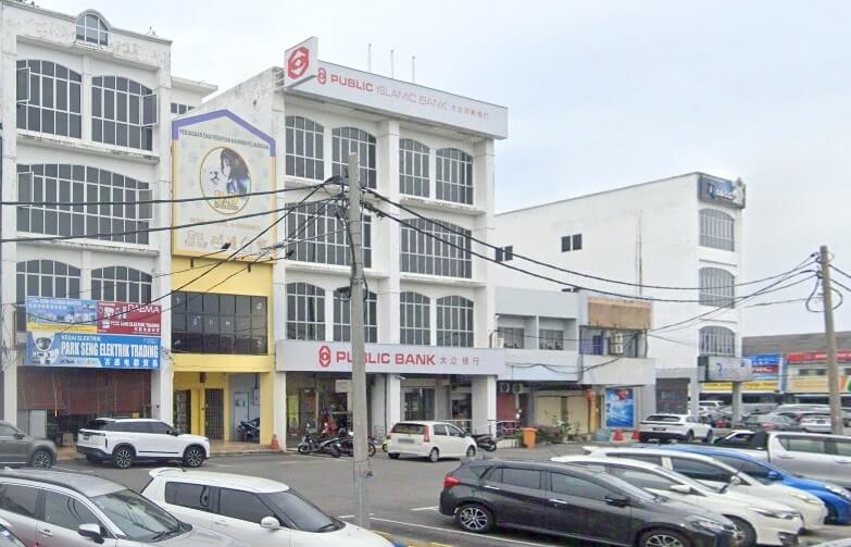 emandangan jalan deretan rumah kedai komersial di Sekinchan, Malaysia, menunjukkan cawangan Public Bank dan Public Islamic Bank, dengan kawasan parkir yang sibuk penuh dengan kereta di latar depan