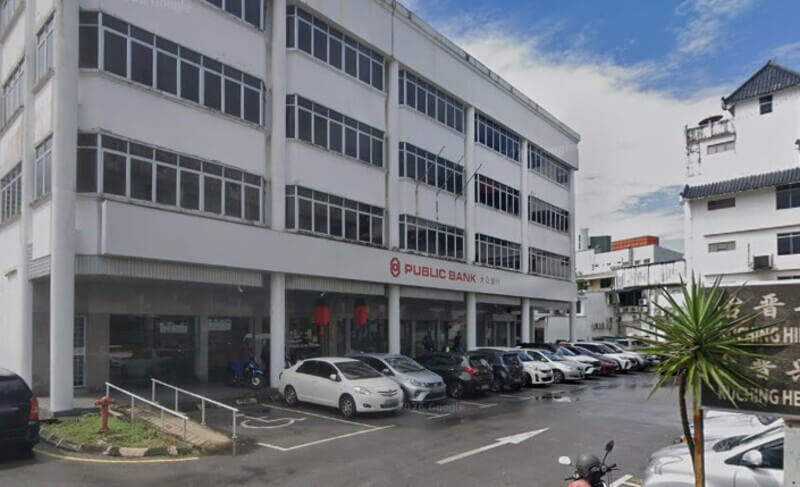 Pemandangan luar bangunan cawangan Public Bank empat tingkat di Kuching dengan deretan kereta diletakkan di tempat letak kereta di hadapannya.