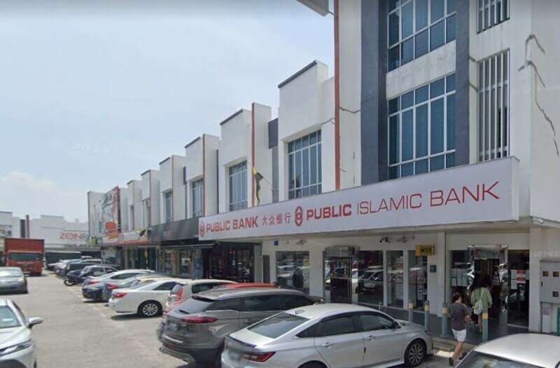 Pemandangan luar cawangan Public Bank dan Public Islamic Bank di deretan kedai dengan deretan kereta diletakkan di hadapannya.