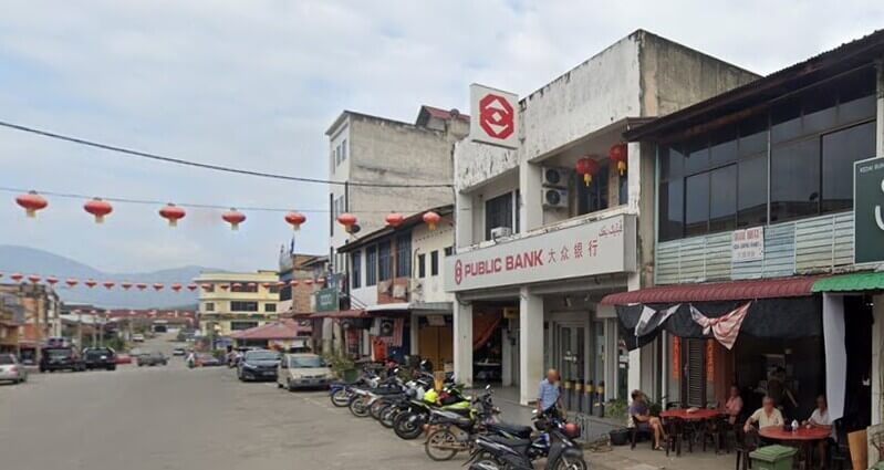 Pemandangan tepi jalan bangunan cawangan Public Bank Kemayan dua tingkat di sebuah deretan kedai rumah dengan tanglung merah digantung di sepanjang jalan.