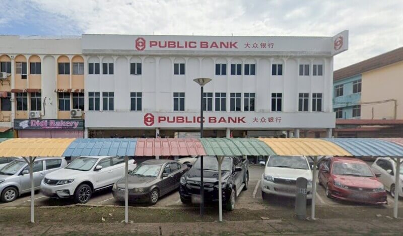 Pandangan hadapan bangunan tiga tingkat berwarna putih milik Public Bank di Limbang, menampilkan papan tanda nama bank serta beberapa kereta yang diparkir di bawah kanopi parkir berwarna-warni di ruang hadapannya.