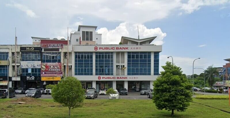 Bangunan cawangan Public Bank Medan Sentral tiga tingkat dengan papan tanda merah, terletak di barisan kedai rumah di tepi jalan pada siang hari.