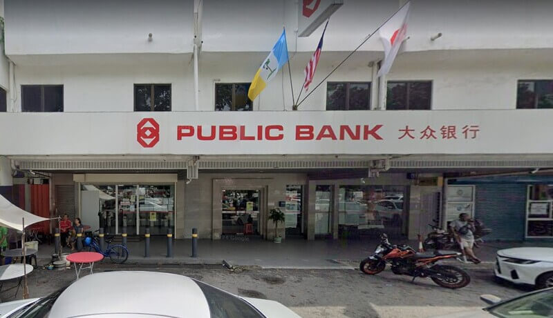 Pandangan hadapan cawangan Public Bank Sungai Nibong dengan papan tanda logo bank, tulisan "PUBLIC BANK" serta tulisan Cina, dan bendera-bendera yang berkibar di atas bangunan.