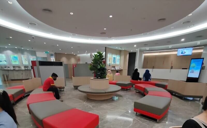 Pemandangan ruang dalaman cawangan Public Bank di Jalan Raja Chulan yang moden, menampilkan kawasan menunggu dengan tempat duduk melengkung berwarna merah dan kelabu serta kaunter perkhidmatan.