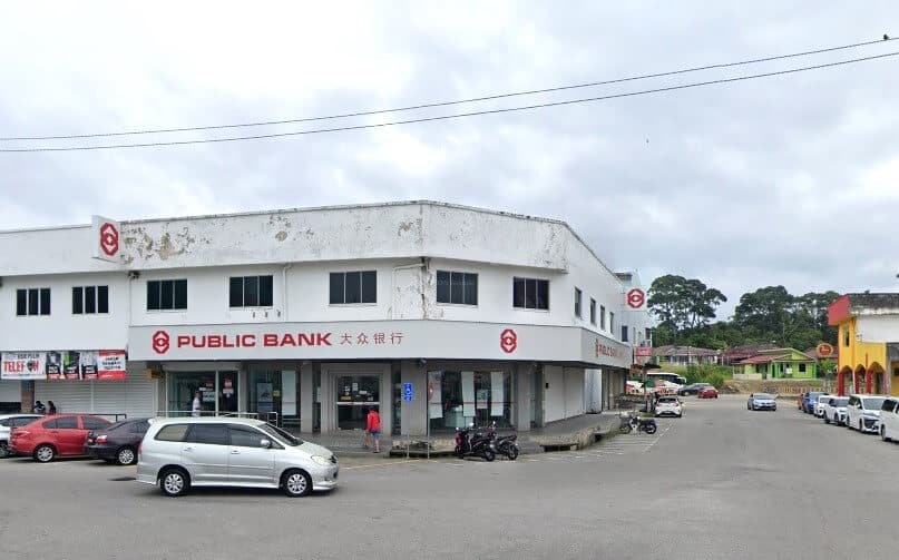 Bahagian luar cawangan Public Bank Masjid Tanah, bangunan komersial dua tingkat dengan fasad putih pudar dan tingkap berbingkai hitam. Nama bank itu, 'PUBLIC BANK', dan aksara Cinanya dipaparkan dengan jelas dengan warna merah di atas tingkap tingkat bawah