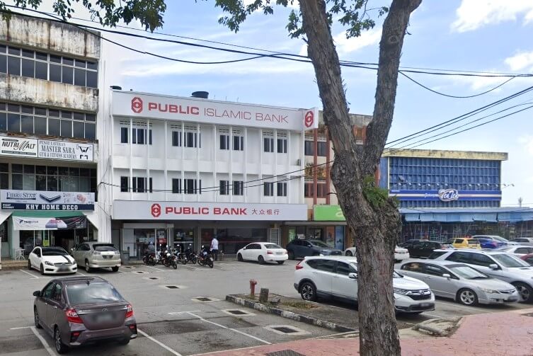 Eksterior cawangan Public Bank di kawasan komersial di Port Dickson. Bahagian luar bangunan putih tiga tingkat menempatkan cawangan Public Bank, dengan papan tanda "PUBLIC ISLAMIC BANK" di dinding tingkat atas dan "PUBLIC BANK" di tingkat bawah. Bangunan ini diapit oleh bangunan komersial lama, termasuk bangunan bertingkat di sebelah kiri