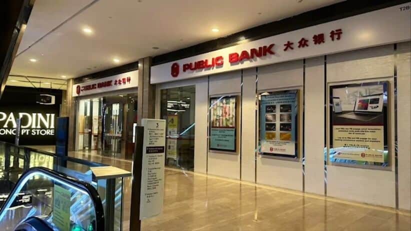 Bahagian luar cawangan Public Bank, terletak di dalam pusat beli-belah moden di Genting Highlands, Malaysia. Nama bank itu dipaparkan dengan jelas dalam skrip merah Inggeris dan Mandarin. Poster promosi tergantung di tingkap, dan eskalator serta etalase lain (Padini Concept Store) kelihatan di sebelah kiri