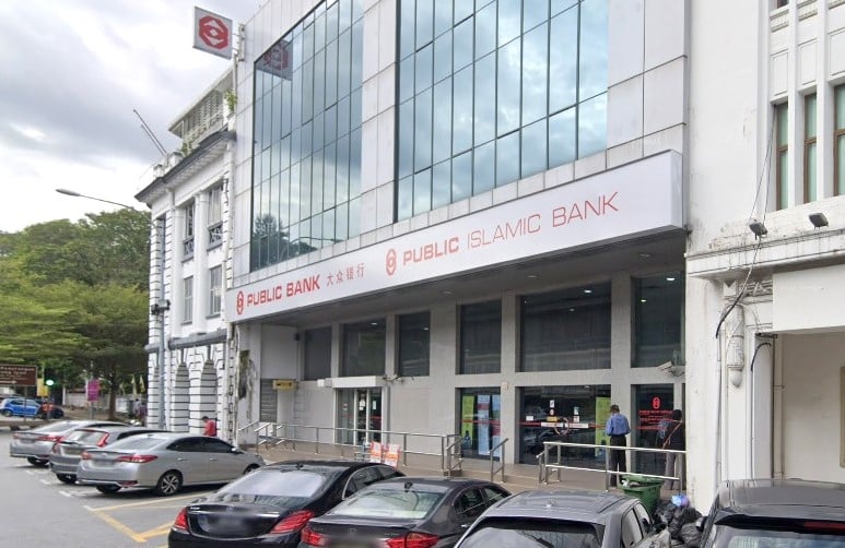 Pemandangan jalan bangunan Public Bank Ipoh Main Office. Bangunan ini mempunyai bahagian moden dengan fasad kaca besar yang memaparkan tanda "PUBLIC BANK" dan "PUBLIC ISLAMIC BANK" dalam huruf putih dan merah, bersama dengan logo bank
