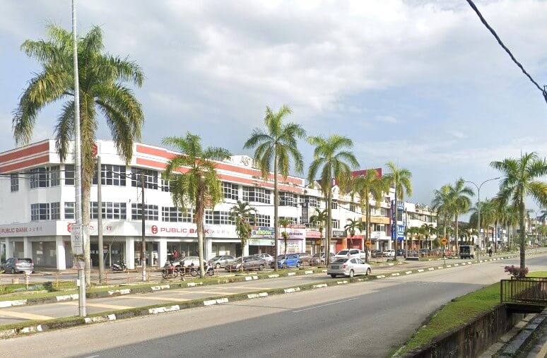 Pemandangan jalan di kawasan komersial di Kamunting, Malaysia. Bahagian kiri imej menunjukkan deretan rumah kedai dua dan tiga tingkat dengan fasad putih dominan dan aksen merah di sepanjang garis bumbung. Bangunan paling menonjol di hujung kiri ialah cawangan Public Bank Kamunting. Terdapat beberapa kedai hadapan lain kelihatan di sepanjang jalan