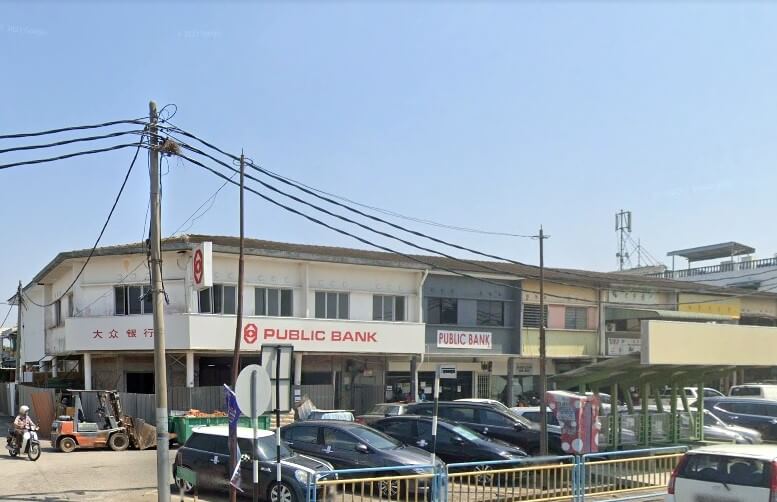 Deretan bangunan komersial bertingkat rendah, menampilkan pejabat Public Bank Kepala Batas, di Malaysia, dengan papan tanda merah dan putihnya. Bangunan-bangunannya adalah gaya lama, dan kawasan letak kereta dengan beberapa kereta terletak di latar depan