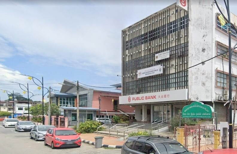 Street view of a Public Bank branch in Kuala Pilah, Malaysia. Bank ini ditempatkan di dalam bangunan berbilang tingkat gaya abad pertengahan dengan fasad berwarna krim, menampilkan papan tanda 'PUBLIC BANK' yang terkenal dan aksara Cina di atas pintu masuk