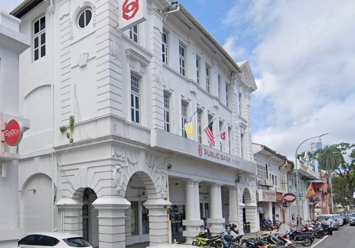 Bangunan bersejarah gaya kolonial putih bertingkat yang menempatkan pejabat Public Bank dengan tingkap melengkung di tingkat bawah, bendera dan pemandangan jalan dengan motosikal yang diletakkan