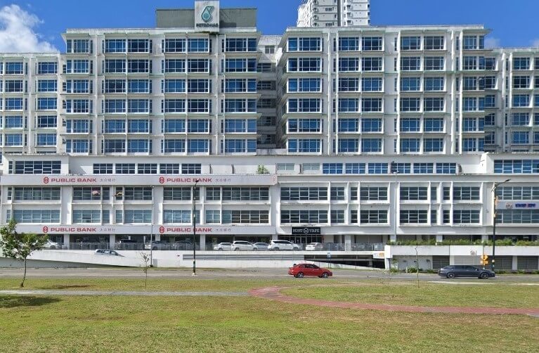 Sebuah bangunan putih bertingkat dengan banyak tingkap segi empat sama. Tiga tingkat bawah adalah cawangan Public Bank Bintulu dengan logo dan nama boleh dilihat dalam bahasa Inggeris dan Mandarin. Logo Petronas terletak di atas bumbung