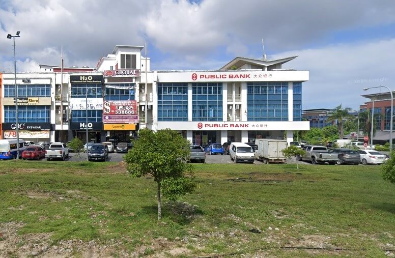 Pemandangan luar bangunan cawangan Public Bank Medan Sentral tiga tingkat dengan tingkap biru, terletak di kawasan komersial dengan hadapan kedai lain, dan kawasan berumput di latar depan