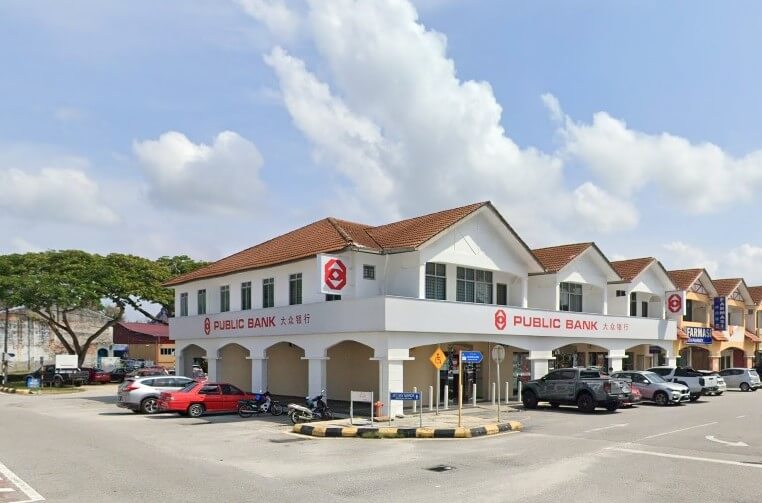 Bahagian luar bangunan cawangan Public Bank dua tingkat di Kuala Selangor, dengan fasad putih, jubin bumbung merah, dan logo Public Bank yang menarik. Kereta dan motosikal diletakkan di kawasan jalan sekitar