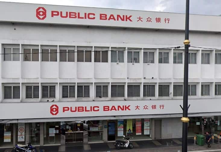 Bahagian luar bahagian tengah cawangan Public Bank di Klang, menampilkan bangunan tiga tingkat berwarna putih dengan beberapa tingkap persegi dan papan tanda merah yang mencolok dalam bahasa Inggeris dan Mandarin di tingkat atas dan bawah