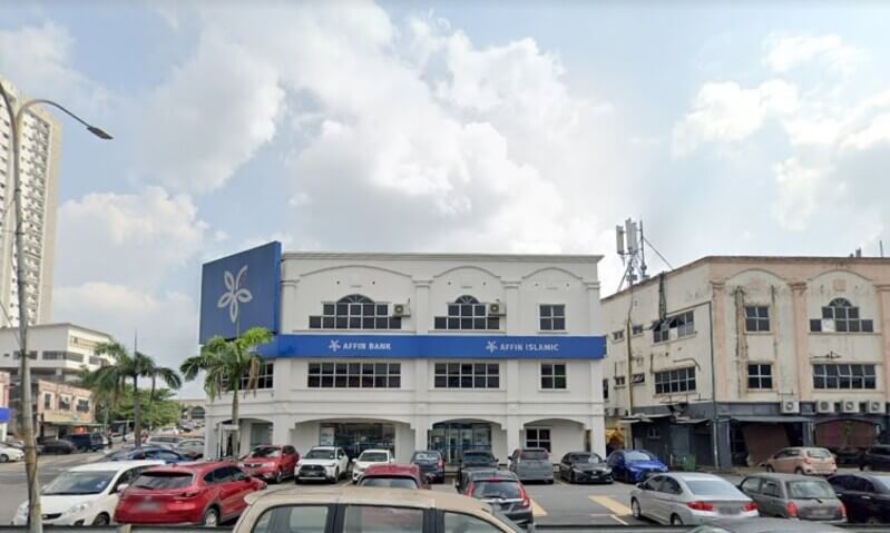 Pemandangan depan bangunan cawangan Affin Bank Seri Kembangan dan AFFIN ISLAMIC dengan papan tanda biru dan logo syarikat, dikelilingi oleh kereta yang diparkir.