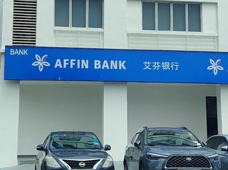 Pemandangan luar bangunan cawangan Affin Bank Setia Alam yang memaparkan papan tanda rasmi berwarna biru, logo orkid, dan tulisan Cina, dengan kenderaan diletakkan di hadapan.