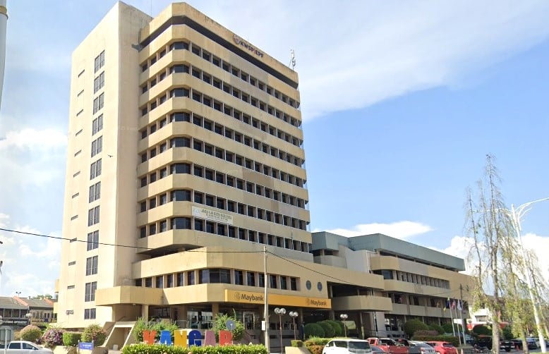 Bangunan bertingkat tinggi berwarna krim dengan deretan tingkap mendatar dan bahagian bawah bersebelahan. Bangunan itu berlabel "KWSP" di bahagian atas dan mempunyai tanda cawangan "Maybank" di tingkat bawah. Ini adalah pejabat KWSP (Employees Provident Fund) di Kangar, Malaysia