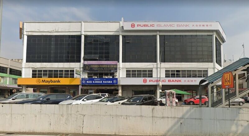 Pemandangan hadapan bangunan perniagaan tiga tingkat yang menempatkan cawangan Public Bank Bandar Puchong Jaya, Public Islamic Bank, Maybank, dan Restoran Nasi Kandar Mafana dengan barisan kereta diletakkan di hadapannya.