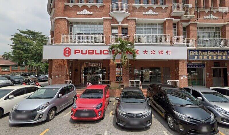Pemandangan hadapan cawangan Public Bank Bandar Sungai Long di bangunan batu bata merah dengan deretan kereta diletakkan di petak letak kereta di hadapannya.