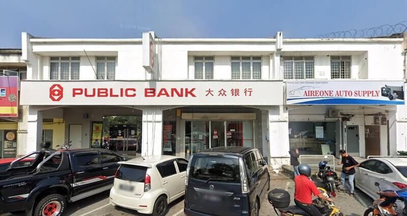 Pandangan hadapan cawangan Public Bank Bukit Beruntung di rumah kedai dua tingkat dengan papan tanda 'PUBLIC BANK 大众银行', bersebelahan kedai Aireone Auto Supply dan beberapa kenderaan diletakkan di hadapan.