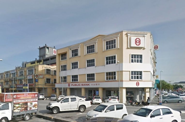 Bangunan komersial empat tingkat kuning muda yang menempatkan cawangan Public Bank di Chukai, Malaysia. Bangunan itu mempunyai aksen putih dan logo dan nama Public Bank berwarna merah di atas tingkat bawah
