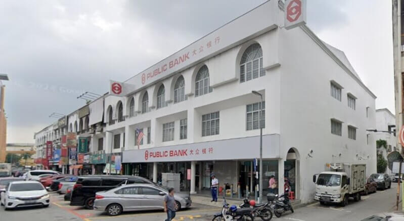 Pemandangan sudut cawangan Public Bank Kajang bangunan putih tiga tingkat di kawasan rumah kedai yang sibuk dengan kenderaan diletakkan di hadapan.