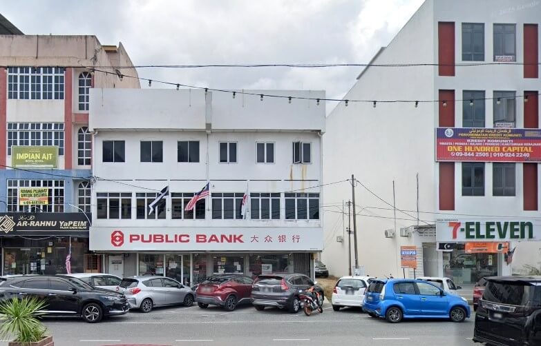 Pemandangan jalan bangunan cawangan Public Bank tiga tingkat di Kuala Dungun, Malaysia. Bangunan putih ini mempunyai tingkap besar di tingkat bawah dan logo serta nama bank itu berwarna merah dan putih dalam kedua-dua bahasa Inggeris dan Mandarin. Bangunan ini diapit oleh bangunan komersial lain, termasuk bangunan empat tingkat di sebelah kanan dengan 7-Eleven di tingkat bawah