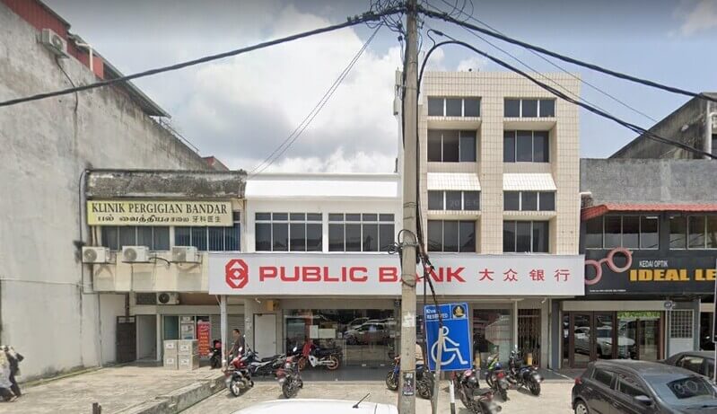 Pandangan hadapan cawangan Public Bank di kawasan kedai Semenyih dengan papan tanda berprestij merah dan putih, diapit oleh Klinik Pergigian Bandar dan kedai optik.