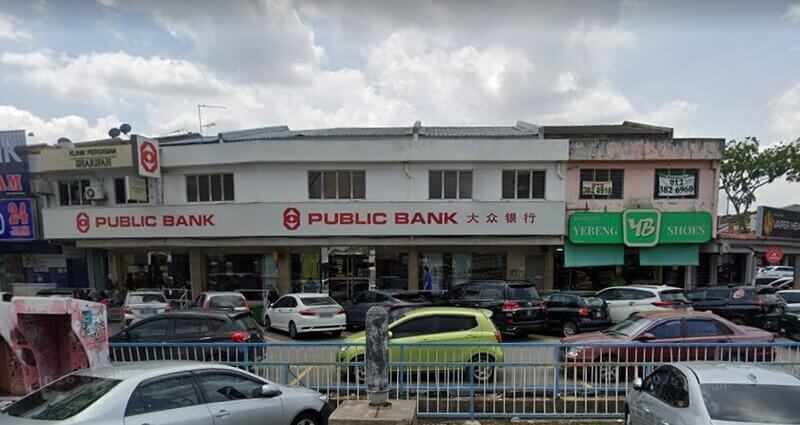 Bangunan kedai dua tingkat yang menempatkan cawangan Public Bank Sungai Buloh dan kedai kasut YEBENG SHOES dengan kawasan tempat letak kereta di hadapannya.