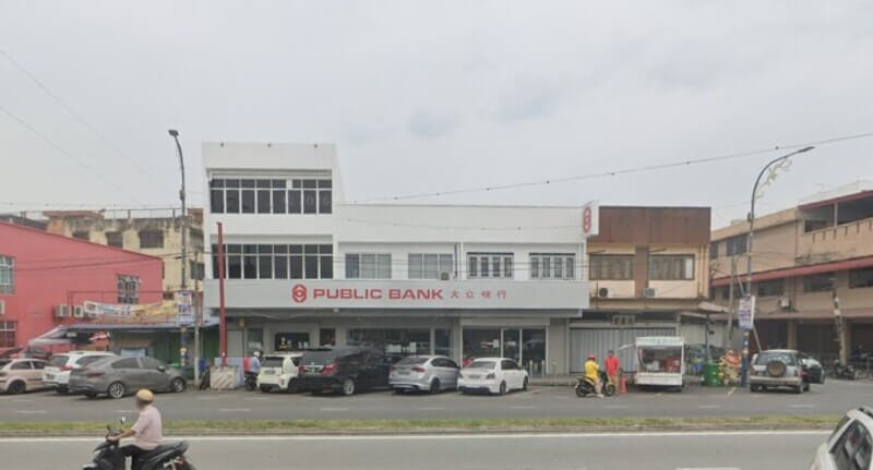 Bangunan cawangan Public Bank berwarna putih di Sungai Jarom dengan papan tanda merah dan barisan kereta di hadapannya.