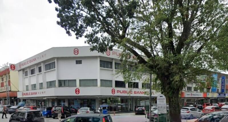 Pandangan luar bangunan cawangan Public Bank Taman Muda dua tingkat berwarna putih di sudut jalan yang dikelilingi kenderaan dan pokok rendang.