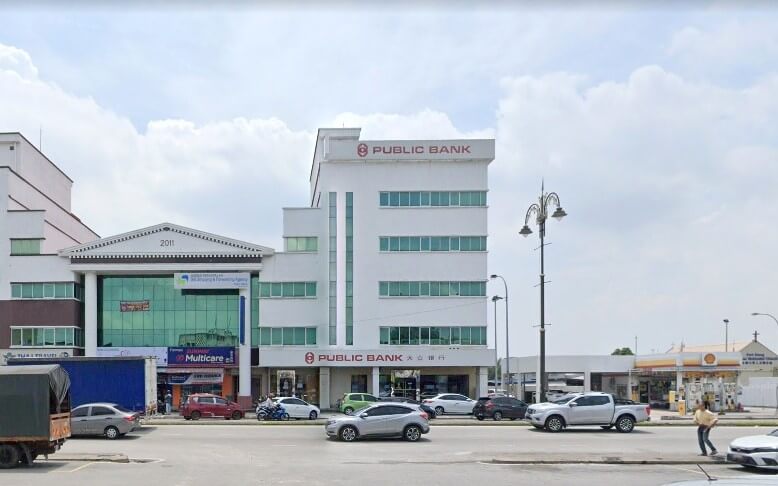 Bahagian luar bangunan cawangan Public Bank bertingkat berwarna putih di Pelabuhan Klang, Malaysia, dengan lalu lintas di latar depan dan stesen minyak Shell kelihatan di sebelah kanan