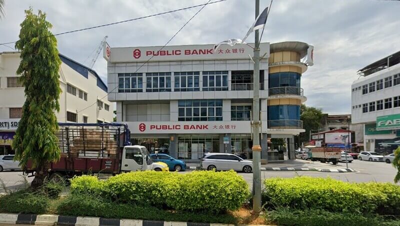 Pandangan hadapan bangunan cawangan Public Bank Kuala Terengganu tiga tingkat dengan papan tanda nama bank dalam tulisan Rumi dan Cina, kelihatan kenderaan dan lanskap pokok di tepi jalan.