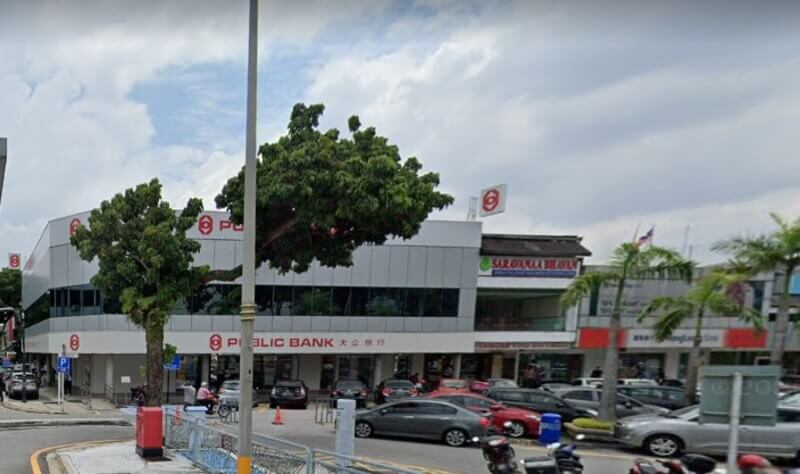 Pemandangan aras jalan cawangan Public Bank Petaling Jaya New Town di kawasan komersial dengan deretan kereta yang diletakkan di hadapannya di bawah cuaca mendung.