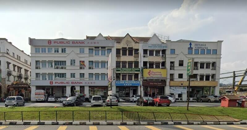 Barisan bangunan kedai tiga tingkat yang menampilkan cawangan Public Bank Taman Indah dan beberapa premis perniagaan lain di tepi jalan bersama deretan kereta terparkir