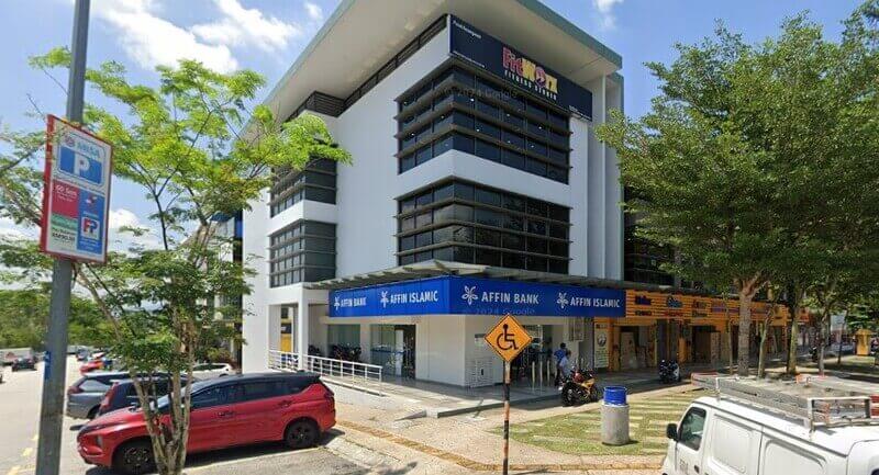 Pandangan luar bangunan komersial cawangan Affin Bank Denai Alam dan Affin Islamic di sudut jalan, memperlihatkan papan tanda biru bank, lot kedai bersebelahan, papan tanda tempat letak kereta, serta beberapa kenderaan di kawasan sekitar.