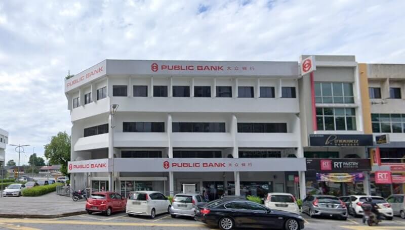 Bangunan cawangan Public Bank Damansara Utama berwarna putih dengan papan tanda merah dan deretan kereta di tempat letak kereta.