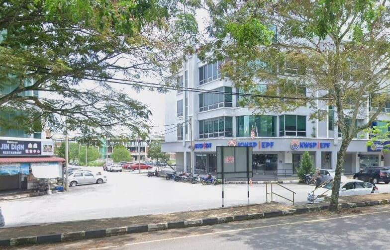 Bangunan pejabat KWSP Taiping di Malaysia, bangunan moden bertingkat dengan tingkap pemantul biru. Fasad tingkat bawah mempunyai tingkap besar dan memaparkan logo dan huruf KWSP EPF berwarna biru dan putih. Di latar depan, terdapat kawasan parkir berturap dengan beberapa kereta dan motosikal. Di sebelah kiri, bangunan satu tingkat menempatkan "Restoran Jin Dian."