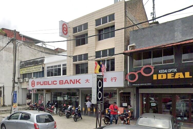 Cawangan Public Bank Semenyih di Selangor, Malaysia, bangunan bertingkat dengan fasad berjubin coklat muda, dikelilingi rumah kedai lain termasuk 'Kedai Optik Ideal Lens' di sebelah kanan. Motosikal diletakkan di hadapan