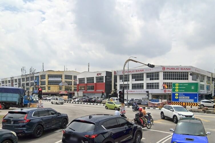 Pemandangan persimpangan yang sibuk, menunjukkan bangunan sudut besar yang diduduki oleh Public Bank and Public Islamic Bank, serta bangunan di sebelahnya dengan papan tanda KFC. Trafik bergerak melalui persimpangan
