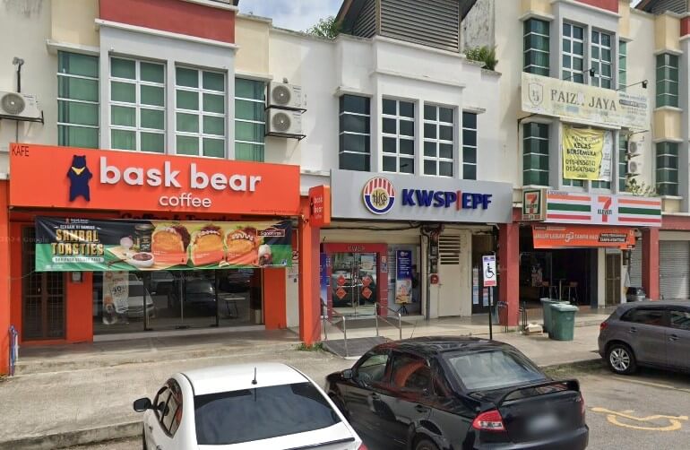 Pemandangan jalan pejabat cawangan KWSP Jasin di Malaysia, terletak di antara kedai Bask Bear Coffee dan kedai serbaneka 7-Eleven. Dua buah kereta diletakkan di hadapan kedai-kedai itu