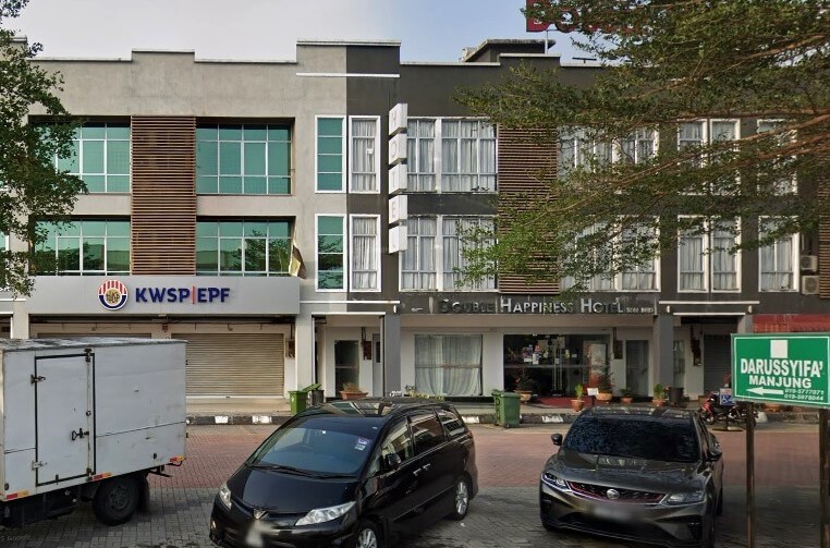 Kompleks bangunan perdagangan tiga tingkat. Bahagian kiri, dengan fasad kelabu dan coklat, memaparkan logo dan papan nama KWSP/EPF (Employees Provident Fund). Sebelah kanan ialah Double Happiness Hotel. Beberapa buah kereta parkir di hadapan, dan kelihatan papan tanda berwarna hijau yang bertulis DARUSSYIFA MANJUNG di hujung kanan