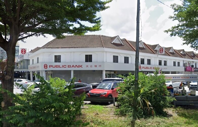 Sebuah bangunan komersial dua tingkat atau bertingkat rendah dengan bumbung jubin coklat dan fasad putih, menempatkan cawangan Public Bank yang boleh dilihat di tengah dan kanan