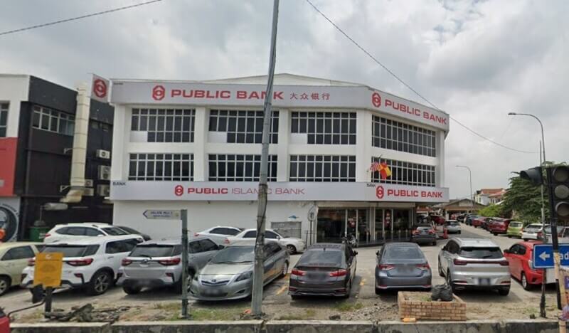 Pemandangan hadapan bangunan cawangan Public Bank Sungai Chua tiga tingkat dengan papan tanda Public Bank dan Public Islamic Bank, serta barisan kereta yang diparkir di hadapannya.