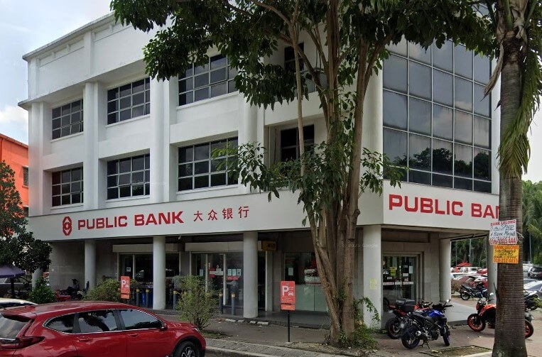 ahagian luar bangunan cawangan Public Bank putih tiga tingkat, dengan namanya dalam huruf Inggeris dan Mandarin merentasi muka bangunan, sebahagiannya dilitupi oleh pokok hijau