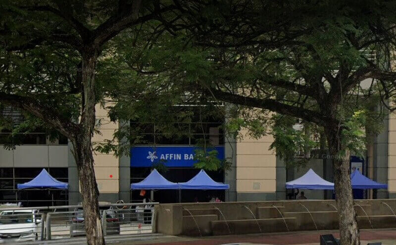 Pandangan luar cawangan Affin Bank di Putrajaya, sebahagiannya dikaburkan oleh pokok-pokok hijau dengan khemah promosi biru dipasang di hadapan