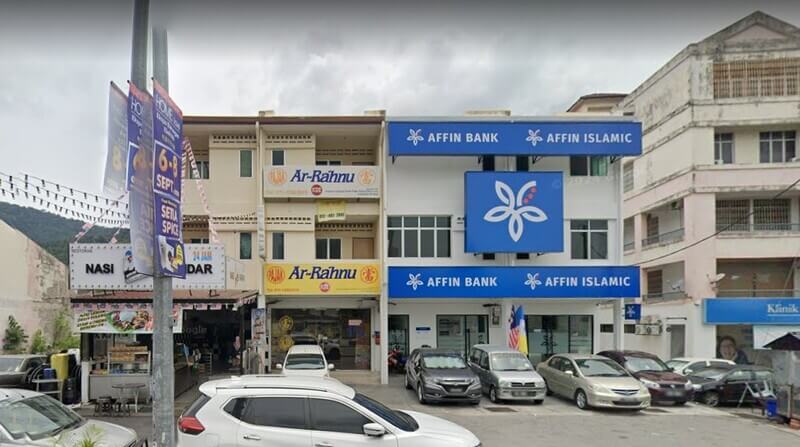 Pandangan hadapan deretan kedai tiga tingkat yang menempatkan cawangan AFFIN BANK Air Itam dan AFFIN ISLAMIC berhampiran kedai Ar-Rahnu, dengan beberapa buah kereta diletakkan di bahagian hadapan.