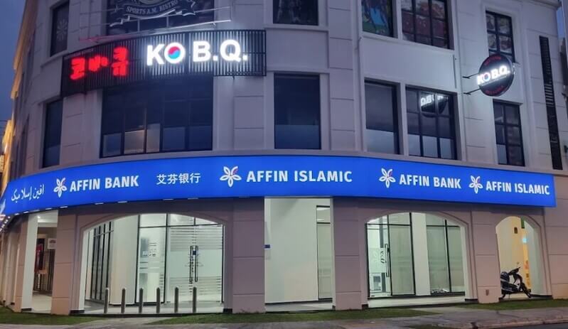 Pandangan hadapan cawangan Affin Bank di Bandar Cassia dan Affin Islamic berlampu di tingkat bawah bangunan komersial pada waktu malam, dengan restoran KO B.Q. di tingkat atas